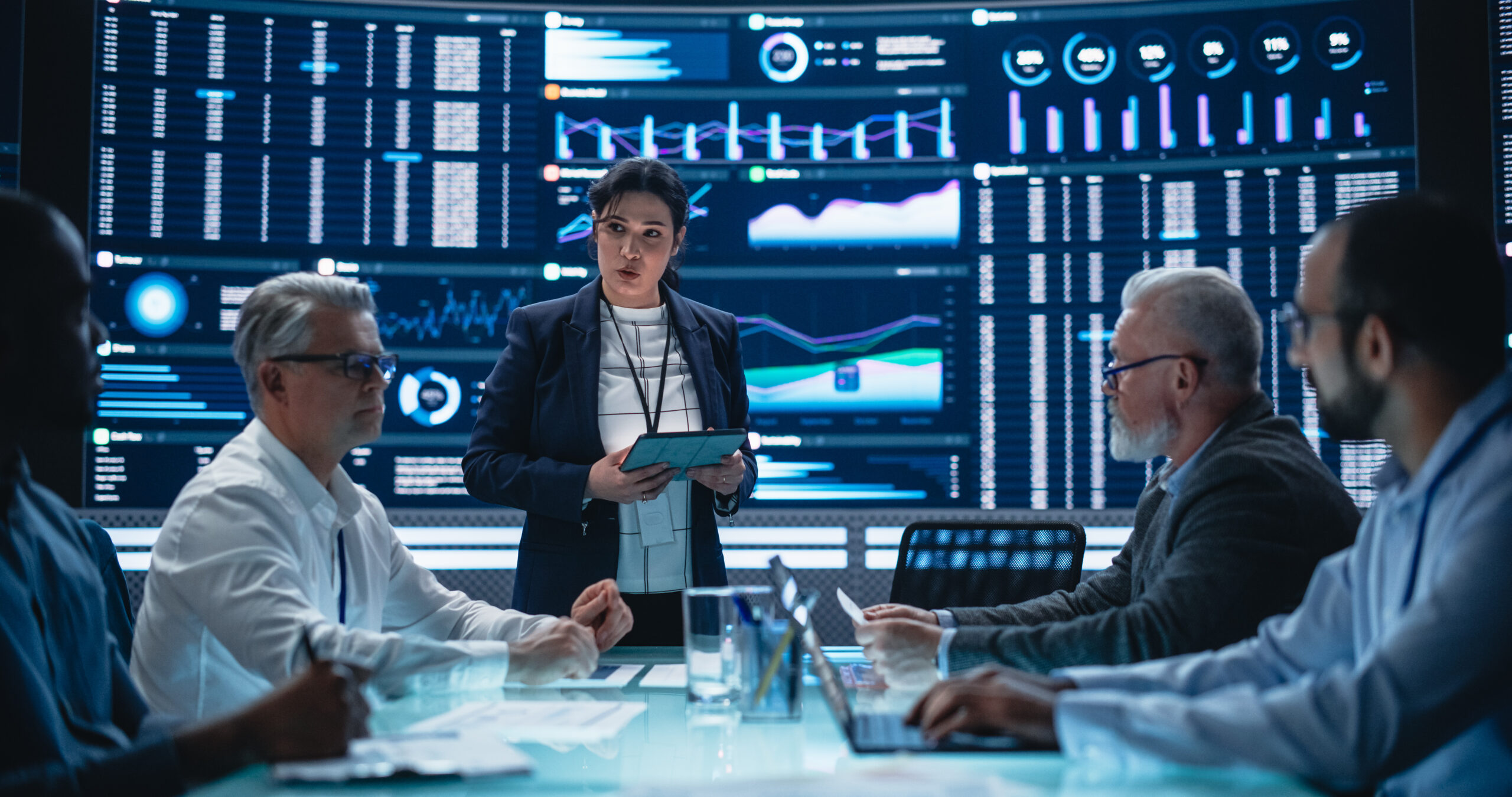 Multiethnic Chief Financial Officer Holding a Meeting with a Group of Fintech Investors. Diverse Team of Managers, Analysts and Board Members Having a Meeting in Front of Big Digital Screen